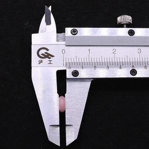 Misurazione di una perla in pietra rosa da 6mm con un calibro in metallo su fondo nero