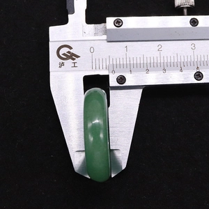 Macro detail of natural green jade ring width being measured with a metal caliper