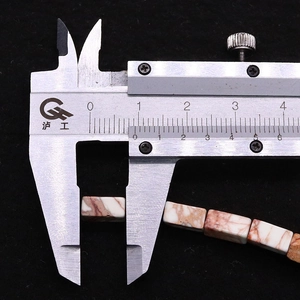 Macro shot of rectangular white turquoise stone beads measured by a caliper on black fabric