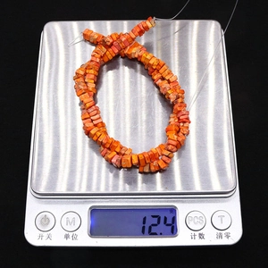 Macro-opname van 4x4mm vierkante oranje natuursteen kralen gewogen op een weegschaal
