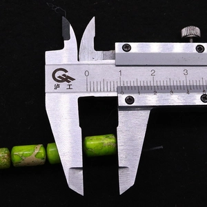 Gros plan de perles tubes en pierre impériale verte de 13mm mesurées au pied à coulisse