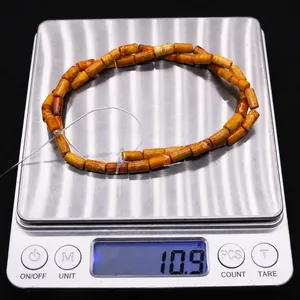 Detail shot of orange cylinder stone beads weighing 10.9g on a digital scale