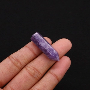 Macro view of natural purple amethyst crystal hexagonal column held between fingers
