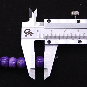 Makroaufnahme einer 10mm flachen lila Kaiserstein-Perle beim Messen mit dem Messschieber