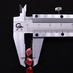 Dettaglio della misurazione di una perla di turchese rosso con un calibro inossidabile