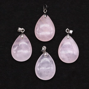 Detail of four pink quartz teardrop pendants with silver clasps on black velvet surface