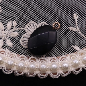 Primer plano del colgante ovalado negro facetado con anillo dorado sobre encaje