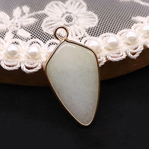 Détail d'un pendentif en pierre naturelle vert clair en forme de bouclier avec bordure dorée
