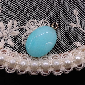 Detalle del colgante ovalado de piedra natural azul claro con anillo dorado sobre encaje