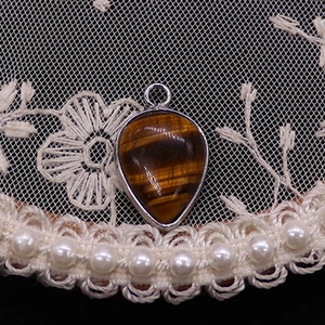 Detail of waterdrop tiger eye pendant with silver frame on vintage lace and pearl decor