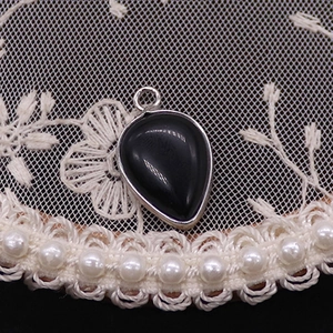 Macro shot of a teardrop black agate pendant with silver metal frame on lace background