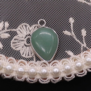 Macro shot of green teardrop stone pendant with silver metal bezel on lace background