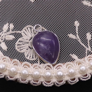 Macro shot of purple teardrop crystal pendant with silver metal edge and ring