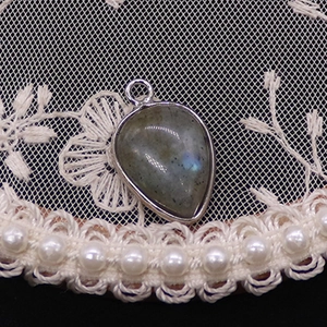 Close-up of a pear-shaped grey labradorite pendant with blue sheen and silver metal rim