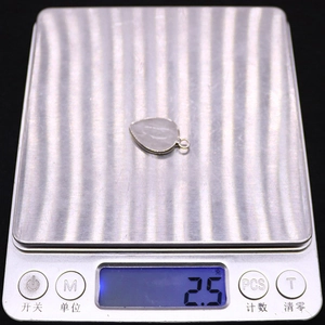 Weight measurement of leaf-shaped silver metal pendant showing 2.5g on a scale