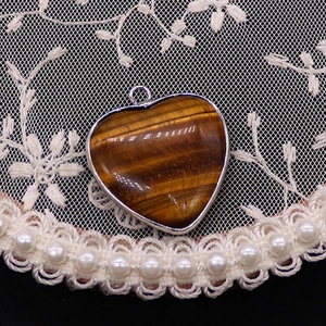 Detailopname van hartvormige tijgeroog hanger met zilveren rand op kant en parel achtergrond