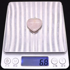 Detailweergave van een hartvormige rozenkwarts hanger van 6,8 g op een weegschaal
