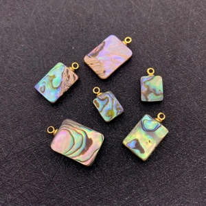 Détail de six pendentifs rectangulaires en nacre d'abalone avec attaches dorées pour bijoux
