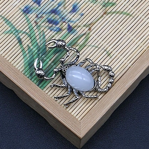 Detalle de colgante de escorpión con piedra blanca en metal plateado antiguo