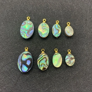 Lot de huit pendentifs ovales en nacre d'abalone avec anneaux dorés sur fond noir