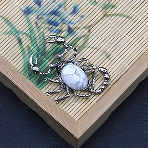 Detalle de un colgante de escorpión plateado con incrustación de piedra de mármol blanco