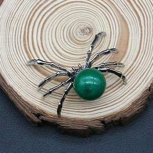 Macro shot of spider-shaped pendant with a green gemstone on a natural wood slice