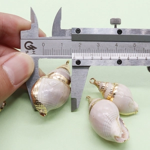 Vue macro d'un pendentif en coquillage naturel avec bordure dorée mesuré au pied à coulisse