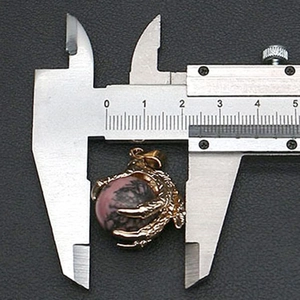 Macro shot of a dragon claw pendant holding a pink marble stone measured by a caliper