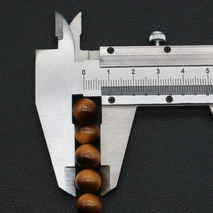 Calipers measuring the diameter of brown round glass tiger eye beads for DIY jewelry