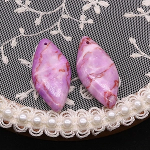 Primer plano de colgantes marquesa de piedra púrpura con vetas rojas sobre encaje blanco