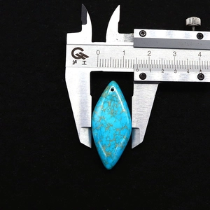 Mesure de la largeur d'un pendentif en turquoise avec un pied à coulisse en métal