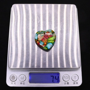 Macro che mostra il peso di 7,4 grammi di un ciondolo in pietra a forma di cuore colorato