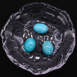 Tres piedras turquesas ovaladas con vetas doradas en un plato de vidrio texturizado