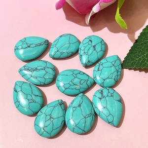 Flat lay of ten teardrop-shaped turquoise stones with black veins on a pink floral background
