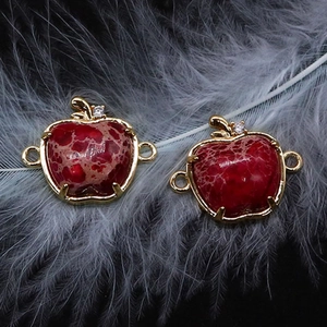 Détail de pendentifs en pierre rouge en forme de pomme avec bords dorés et cristaux
