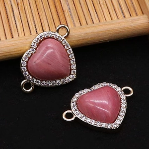 Vue détaillée de deux connecteurs de bijoux en pierre rose en forme de cœur dorés avec zircon