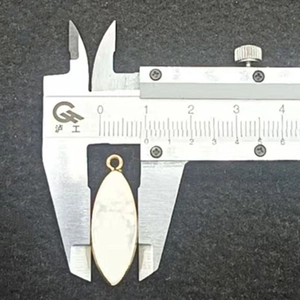 Calipers measuring the 8.5mm width of a gold-plated marquise gemstone pendant