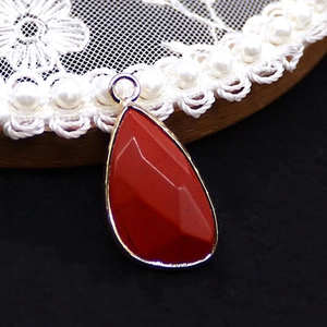 Close-up of faceted red opal teardrop pendant with silver frame on lace base