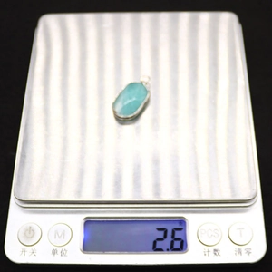 Detailed view of a 2.6g oval green natural stone pendant with silver plated bezel on a scale