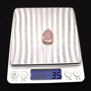 Close-up of pink faceted gemstone pendant with gold plated edge on weighing scale