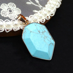 Macro shot of a faceted shield-shaped turquoise pendant with gold plated metal edges