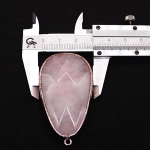 Macro shot showing width measurement of a faceted rose quartz teardrop pendant with gold plating