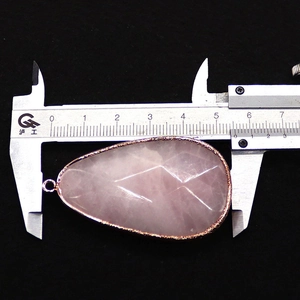 Detail shot of a faceted pink stone teardrop pendant with gold plating measured by a caliper