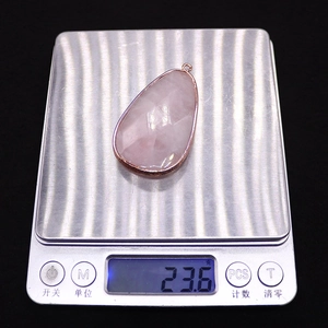 Detailed view of teardrop rose quartz pendant with gold plating on a digital scale