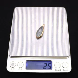Macro shot of a 2.5g natural stone teardrop pendant on a scale with gold plating