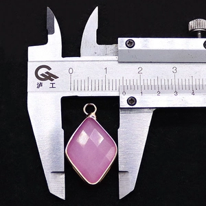 Macro view of a 17mm faceted pink gemstone diamond pendant with gold plated edges and caliper