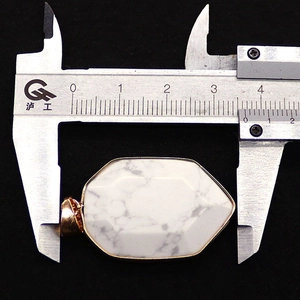 Measuring the width of a shield-shaped faceted white turquoise pendant with gold trim
