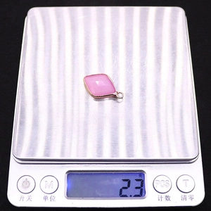 Macro detail of a faceted pink stone pendant in a gold frame on a digital scale weighing 2.3g