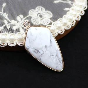 Macro shot of shield-shaped howlite pendant with gold plated trim on lace tray