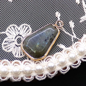 Dettaglio del ciondolo in labradorite sfaccettata con cornice dorata su pizzo e perle